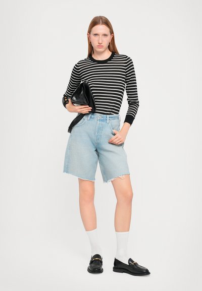 Camicia a maniche lunghe a righe bianco e nero, pantaloni corti di jeans azzurri con orli sfrangiati, pochette nera, mocassini neri e calzini bianchi.