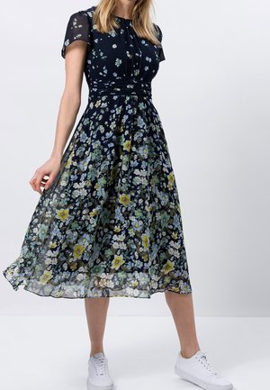 Vestido midi floral con mangas cortas, fondo azul marino, flores vibrantes en amarillo y azul, cintura ceñida y tela ligera y translúcida.