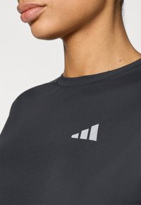 Μαύρο εφαρμοστό t-shirt από μαλακό ύφασμα, με μικρό λευκό τριγωνικό λογότυπο στο επάνω αριστερό μέρος κοντά στο λαιμό.