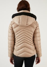 Béžová puffer bunda s čiernou hornou časťou, s chevronovým vzorom na chrbte, dlhými rukávmi a kapucňou. Hladká, lesklá tkanina.