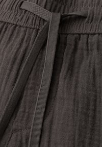 Tissu texturé gris foncé avec une taille élastique et un cordon plat noué en un simple nœud au centre.