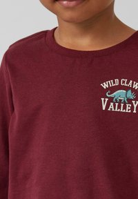 Bordeaux Sweatshirt aus Baumwolle, mit Rundhalsausschnitt, gerippten Bündchen und einem verspielten blauen Dinosaurier-Graphic mit weißem Text.