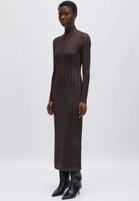 Langes, tailliertes, braunes Kleid mit vertikalen schwarzen Streifen, hohem Kragen, langen Ärmeln und einer glatten Textur, kombiniert mit schwarzen spitzen Stiefeln.