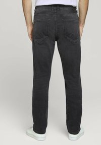 Jeans de mezclilla negra con un corte recto, que cuentan con dos bolsillos traseros y detalles de costura sutiles. Llevados con zapatillas blancas.