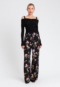 Top off-shoulder a coste nere con dettaglio di bottoni abbinato a pantaloni a palazzo neri a fiori in colori vivaci e a vita alta.