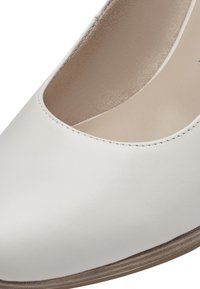 Pompe en cuir blanc avec un bout arrondi, présentant une découpe basse et une texture lisse et légèrement brillante. La semelle extérieure brune apporte un contraste.