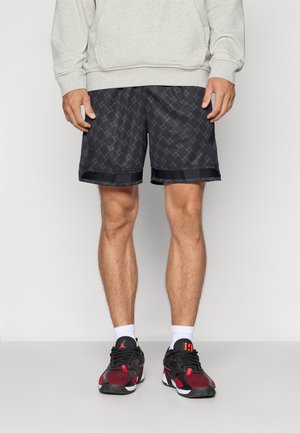 Pantalones cortos negros con un patrón y textura suave, con un borde oscuro contrastante en el dobladillo. Combinados con zapatillas deportivas negras y rojas.