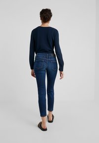 Camiseta de manga larga en color navy combinada con jeans de mezclilla elásticos de color azul oscuro, con un diseño ajustado, cinco bolsillos y una textura suave.