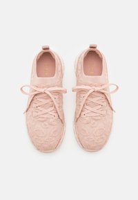 Une paire de baskets tricotées rose pâle avec des lacets et un motif floral subtil, vues de dessus sur un fond blanc.