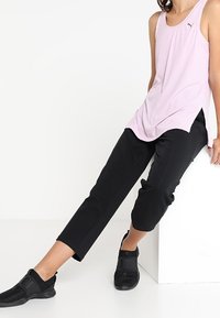 Ljusrosa träningslinne med sidsprund, matchat med svarta snäva byxor och svarta slip-on skor med texturerad ovandel och detaljer.