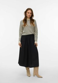 Gonna nera plissettata abbinata a un maglione crema con strisce a chevron nere. La modella indossa stivaletti beige. Texture lisce e design semplice.