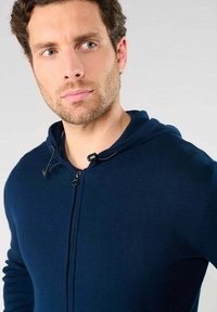 Marineblauwe ritssluiter hoodie met een zachte textuur, voorzien van een trekkoordcapuchon, plastic rits en aansluitende mouwen. Close-up van het bovenlichaam.