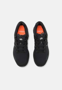 Chaussures de sport noires avec une tige texturée, présentant des accents gris et une semelle intérieure orange vif. Comprend des lacets et un renfort à l'avant.