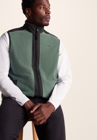 Fleece vest in dark green with black accents, full zip closure, high collar, smooth texture, and logo detail on the chest.