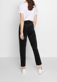 Svarta corduroybyxor med tapered passform, slät textur och standardmidja, kombinerat med en enkel vit t-shirt och vita skor.