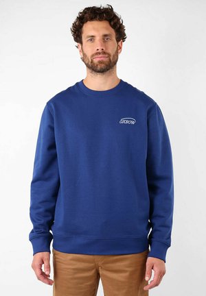 Sweatshirt bleu en coton, avec un col rond, des manches longues, des poignets et un ourlet côtelés, et un petit logo sur la poitrine.