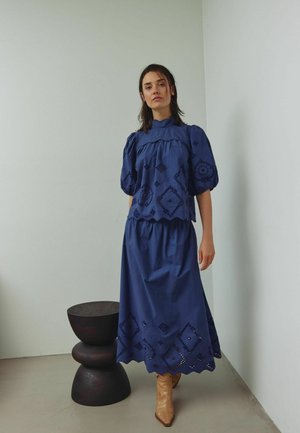 Vestido azul marino con mangas abullonadas, decorado con bordados de diamantes y círculos; diseño en capas con un ligero volante en el dobladillo.