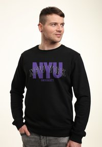 Felpa nera in cotone, caratterizzata da grandi grafiche "NYU" e "NEW YORK UNIVERSITY" in viola e bianco sulla parte anteriore.