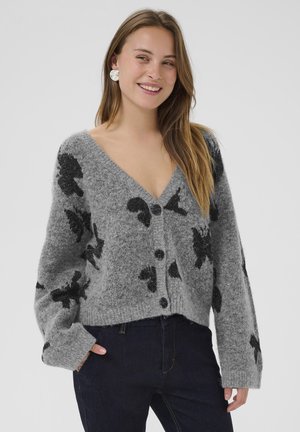 Grau melierter Wollmischungs-Cardigan mit schwarzem abstraktem Muster, tiefem V-Ausschnitt, oversized Ärmeln und Knopfverschluss, getragen mit dunklen Jeans.