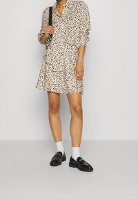 Béžová košile a sukně se vzorem černých teček. Košile je oversized; sukně je rozšířená. Obojí doplněno černými mokasíny a bílými ponožkami.