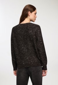 Czarny sweter z dzianiny o luźnym kroju, z metalicznymi błyskami w całej powierzchni, ściągaczami przy mankietach oraz okrągłym dekoltem.