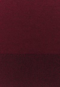 Gros plan sur un tissu tricoté bourgogne avec une ourlet côtelé au bord inférieur.