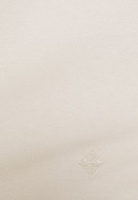 Tessuto a coste di colore crema con un sottile logo ricamato nell'angolo in basso a destra. Texture morbida con linee fini e uniformi.
