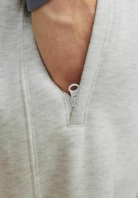 Light gray sweatshirt fabric with a pocket featuring a white zipper. The texture is soft, with a subtle heathered pattern.