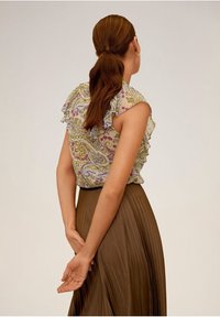 Ärmellose Bluse mit floralem Muster und gerafften Kanten, kombiniert mit einem braunen Faltenrock. Das Outfit hat eine taillierte Taille und eine fließende Silhouette.