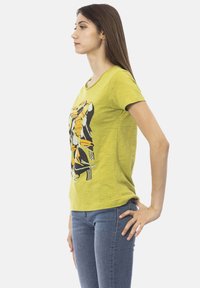 T-shirt di cotone gialla con stampa grafica e accenti neri e arancioni. Maniche corte, scollatura rotonda e vestibilità rilassata.
