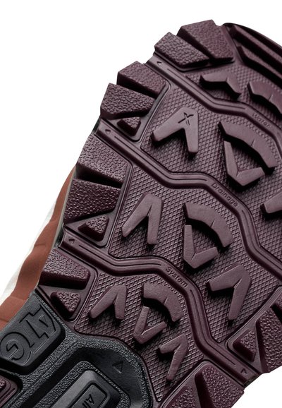 Gros plan sur une semelle de boot marron et noire avec des motifs de crampons profonds et la marque "ATG" sur un fond blanc.