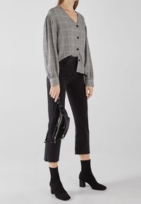 Cardigan grigio a quadri con scollo a V, chiusura con bottoni neri, abbinato a jeans neri a vita alta e stivaletti neri a coste.