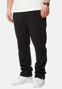 Schwarze Jogginghosen mit einer lockeren Passform, mit einer glatten Textur und Seitentaschen, kombiniert mit weißen Turnschuhen.