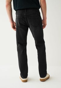 Jeans din denim negri cu croială dreaptă, design cu cinci buzunare și cusături vizibile. Asortați cu adidași albi având o talpă maro.