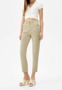 Ljust gröna, högmidjade jeans med rak benform, fem fickor och bältesömmar, ihop med en vit ribbad crop top och beige plattformsskor.