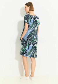 Kurzarmkleid mit einem mehrfarbigen Blättermuster in Blau, Grün und Schwarz; knielang mit seitlichen Taschen und einem Schlüssellochdetail auf der Rückseite.