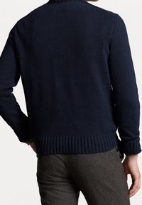 Mörkblå stickad tröja med ribbad nederkant och ärmslut, som har ett strukturerat mönster. Baksidan visar en enkel, klassisk design.