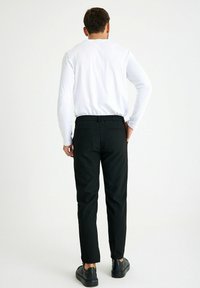 Zwarte broeken met een elastische tailleband, voorzien van twee achterzakken en een toegespitst ontwerp, gecombineerd met een witte long-sleeve shirt.