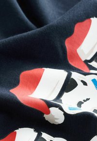 Granatowy materiał o gładkiej fakturze z białym wzorem czaszki w czerwonej czapce świętego Mikołaja i niebieskimi akcentami.