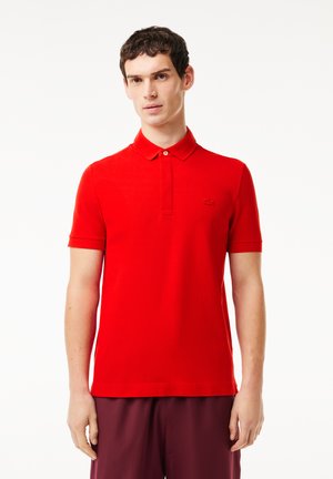 Röd kortärmad polo med knäppkrage, tillverkad av ett texturerat bomullsmaterial och med en liten logotyp på bröstet.