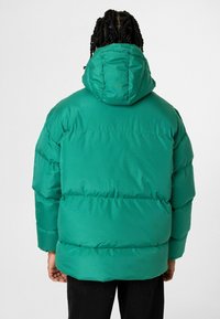 Groene gewatteerde jas met capuchon, voorzien van een quiltpatroon, elastische manchetten en een relaxte pasvorm. Glad, glanzend materiaal met een matte afwerking.