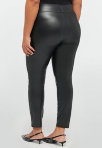 Zwarte neplederen leggings met een soepele textuur en hoge taille, met een aansluitend ontwerp en enkel lengte. Geaccentueerd door gepolijste zwarte schoenen.
