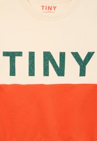 T-shirt à manches courtes avec partie supérieure crème et impression turquoise "TINY" ainsi qu'une partie inférieure orange. Matière en coton, design décontracté.