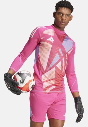 Rosa Langarm-Trikot für Fußballtorhüter mit geometrischen Mustern, kombiniert mit passenden Shorts und schwarzen Handschuhen, während er einen rot-weißen Fußball hält.