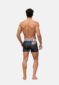 Denimshorts med en blå elastisk midjeband märkt "MUKKO." Synliga bakfickor och en texturerad mörk tvättfinish.