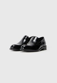 Melnas patentētas ādas slip-on kurpes ar noapaļotu pirkstu, gludu tekstūru un minimāliem akcentiem. Zems papēdis ar zīmola logotipu uz zoles.