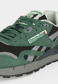 Маратонка Reebok със зелен и черен велур, сиви акценти, зелени връзки, лого Reebok с британското знаме и омекотена сива подметка.