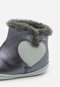 Botte en cuir gris métallique avec finition en fausse fourrure grise, présentant une patch en forme de cœur gris clair et un détail de couture sur la semelle.