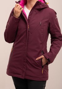 Veste bordeaux avec une doublure rose, dotée d'une fermeture éclair sur le devant, de deux poches latérales et d'une capuche ajustable. Le matériau semble lisse avec une finition légèrement brillante.