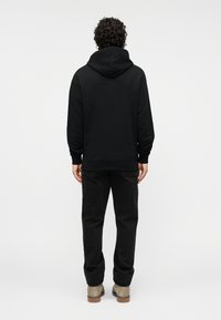 Μαύρο φούτερ με κουκούλα και κορδόνια· φορεμένο με σκούρα παντελόνια· διαθέτει ριμπ μανσέτες και ζώνη στη μέση· απαλή υφή, χαλαρή εφαρμογή.